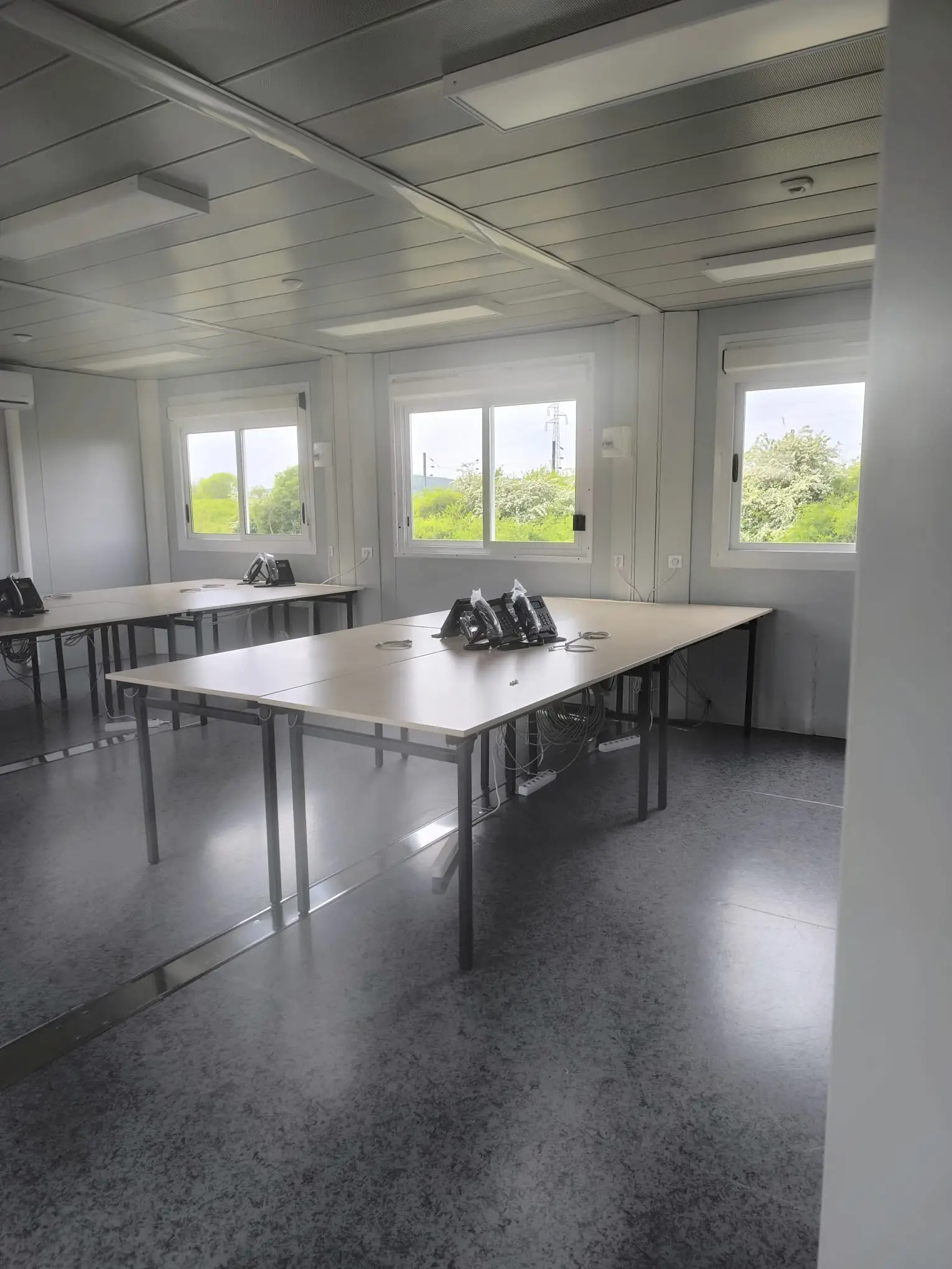 Open space de bureaux modulaires, tables et téléphones installés, sol et vitres propres