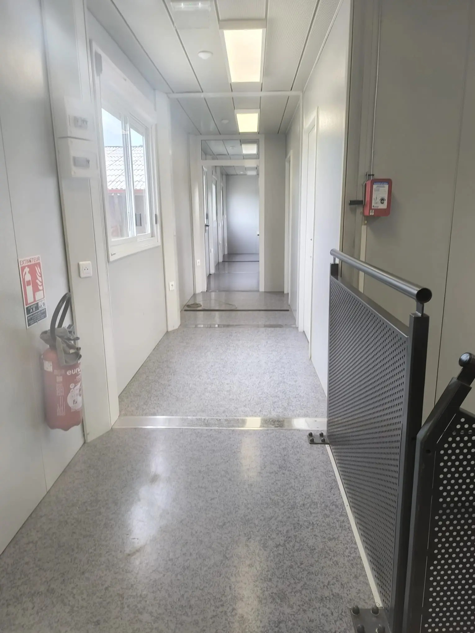 Couloir de bungalows de chantier au sol PVC nettoyé, extincteur au mur
