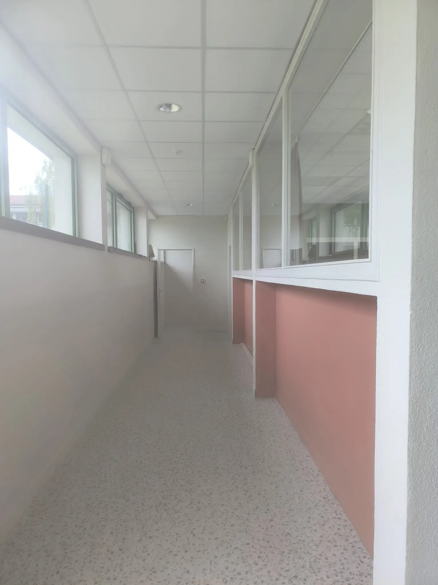 Couloir de bureaux avec cloisons vitrées et sol nettoyé