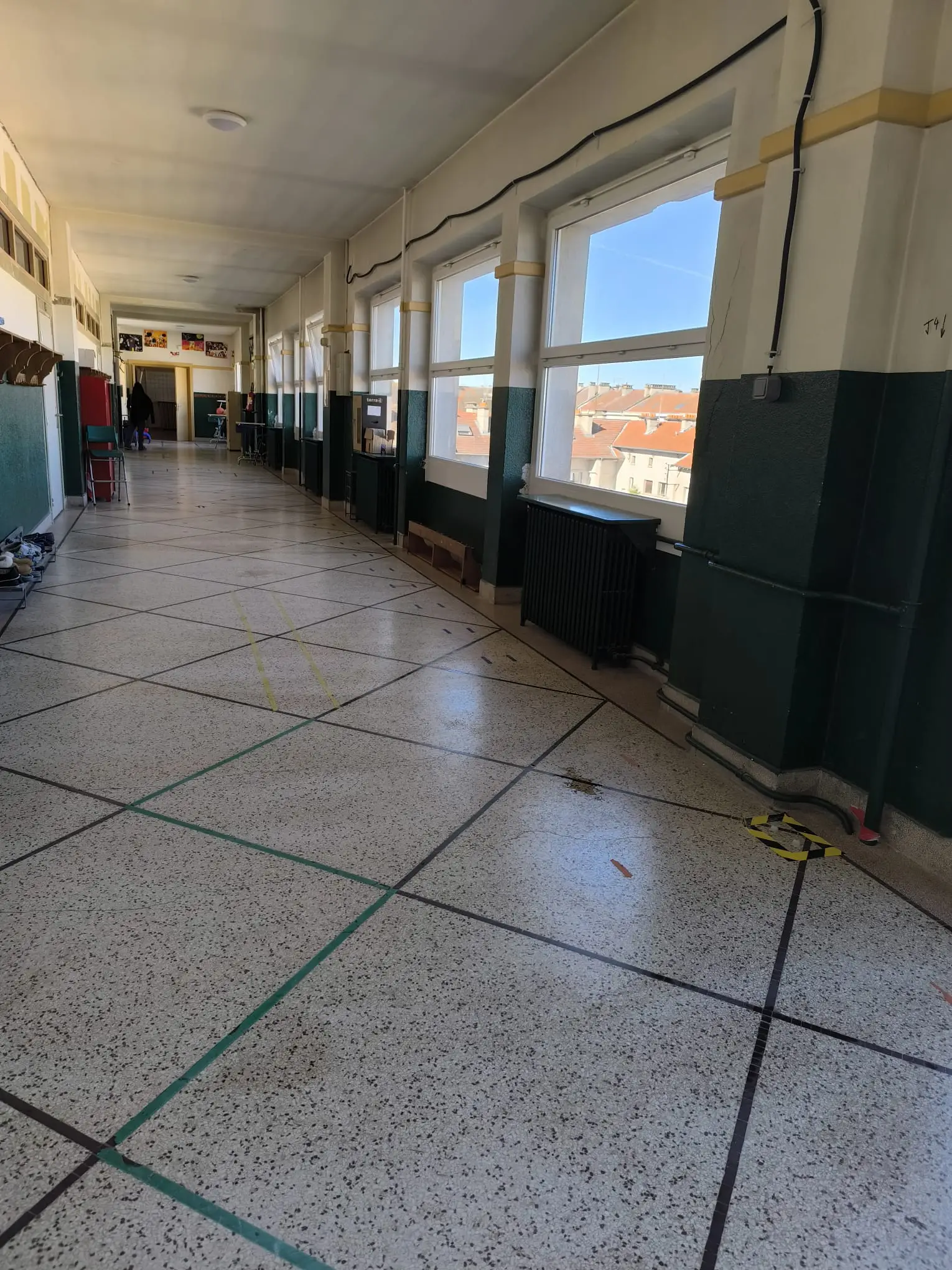 Long couloir d’école au sol granito nettoyé, grandes fenêtres et radiateurs