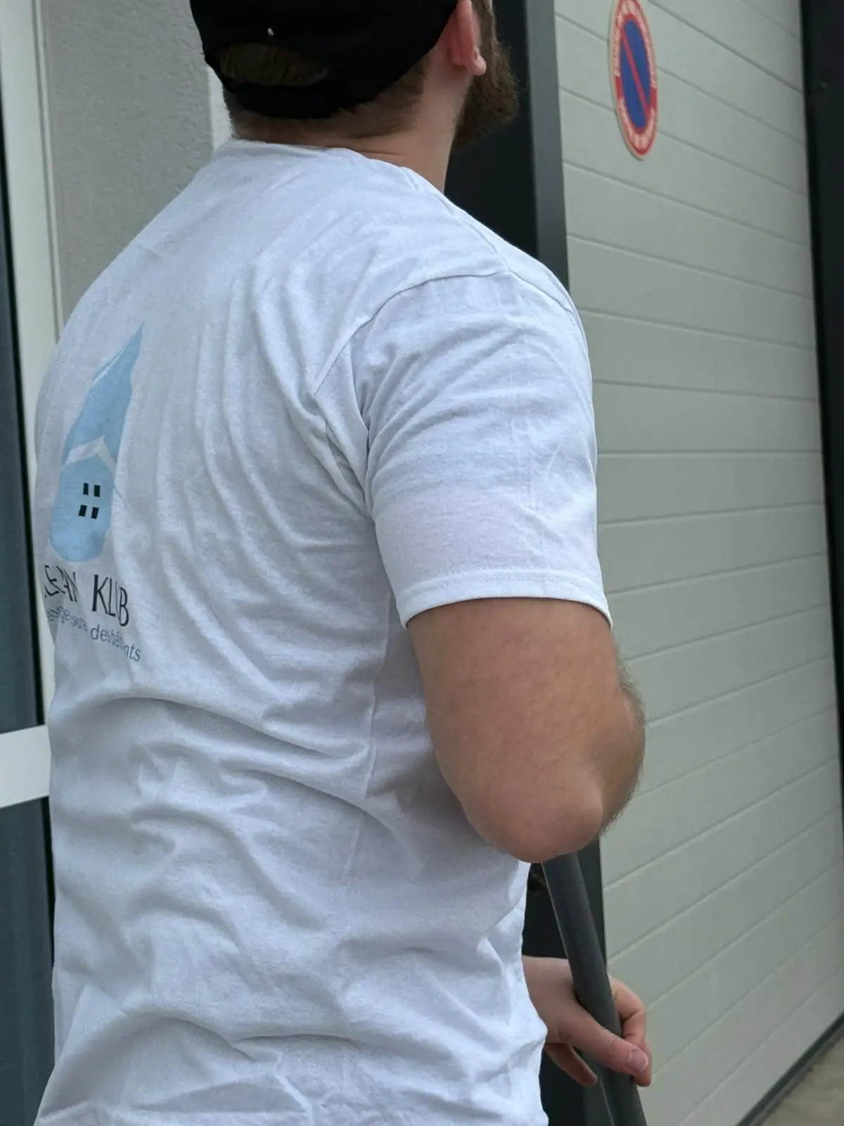 Agent CLEAN KLUB de dos, t-shirt au logo de l’entreprise, devant un bâtiment