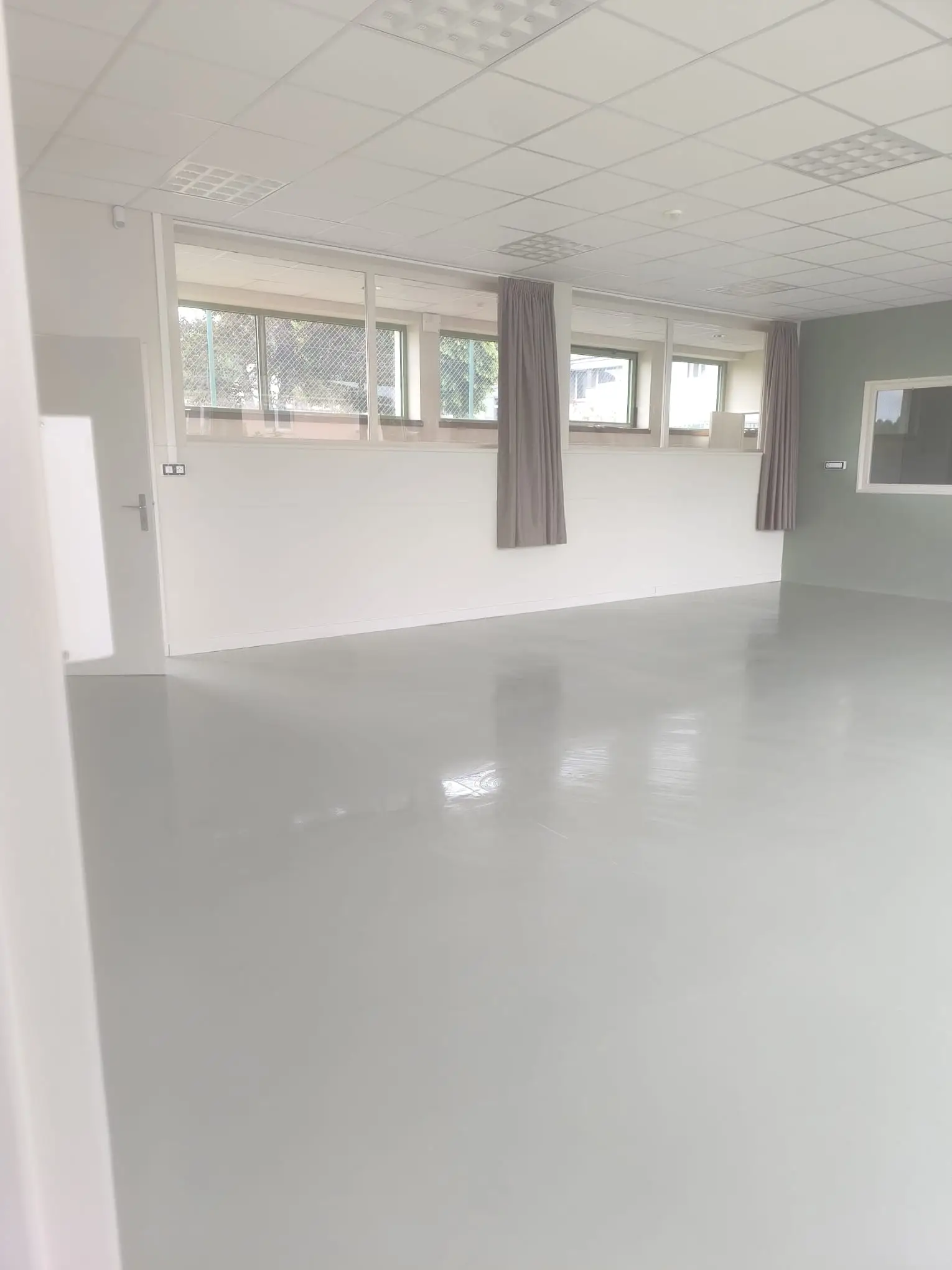 Grande salle vide après travaux, sol gris lustré sans trace, plafond en dalles nettoyé